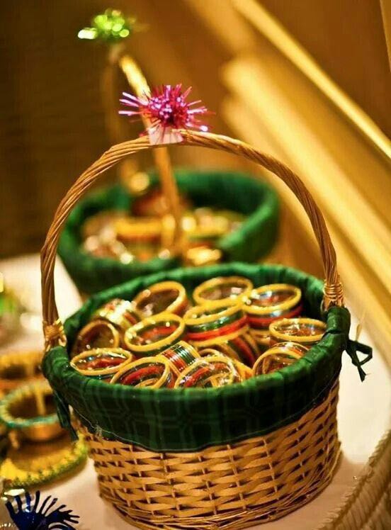 Wicker baskets lined with green cloth holding stacks of glass bangles in red, green and gold, on a white table in warm light