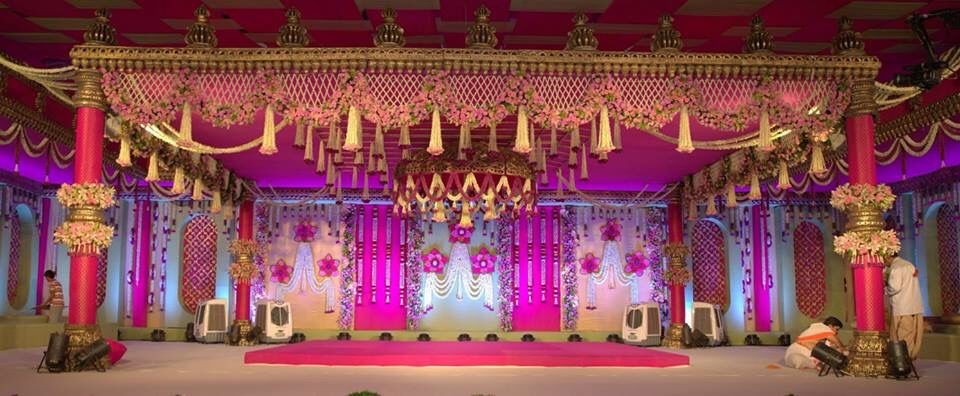 Wide indoor wedding mandap with gold-capped pink pillars, jasmine tassels along the canopy and a pink carpeted stage